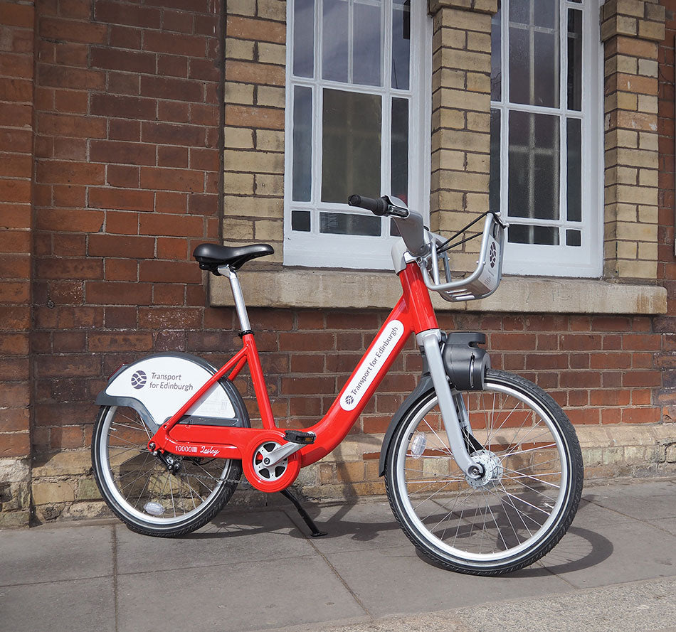 A red Transport for Edinburgh city hire bike outside a train station.