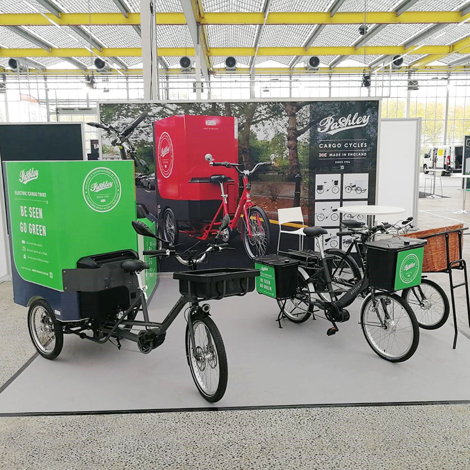 Electric cargo bikes and trikes in green and green in front of large backdrop featuring red cargo bike on London Street.