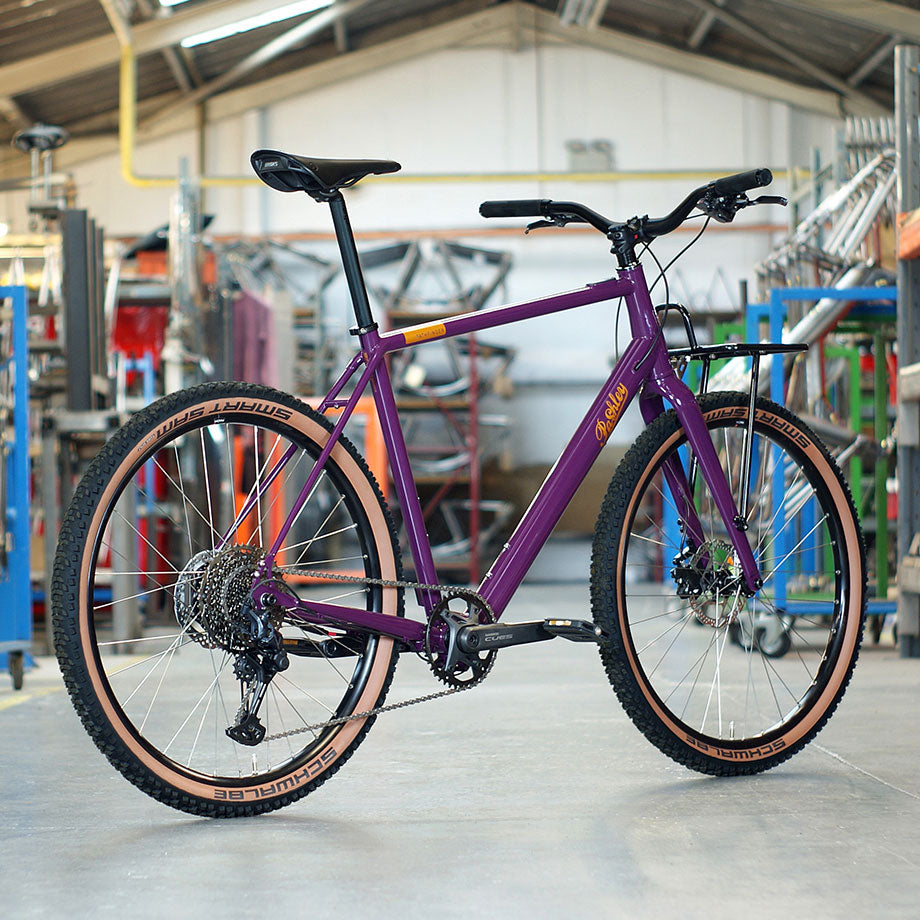 A purple e-bike with black saddle and handlebars, parked on a grey floor within the Pashley factory