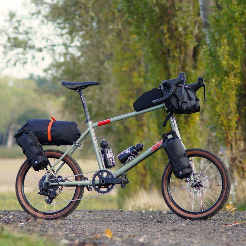 Pashley Skyline Mini-Velo on a gravel path with greenery behind. The bike is packed with black luggage.