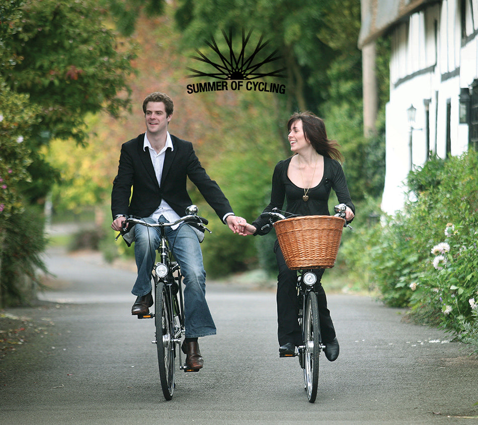 Young couple holding hands whilst cycling Pashley bicycles along a country lane in England.