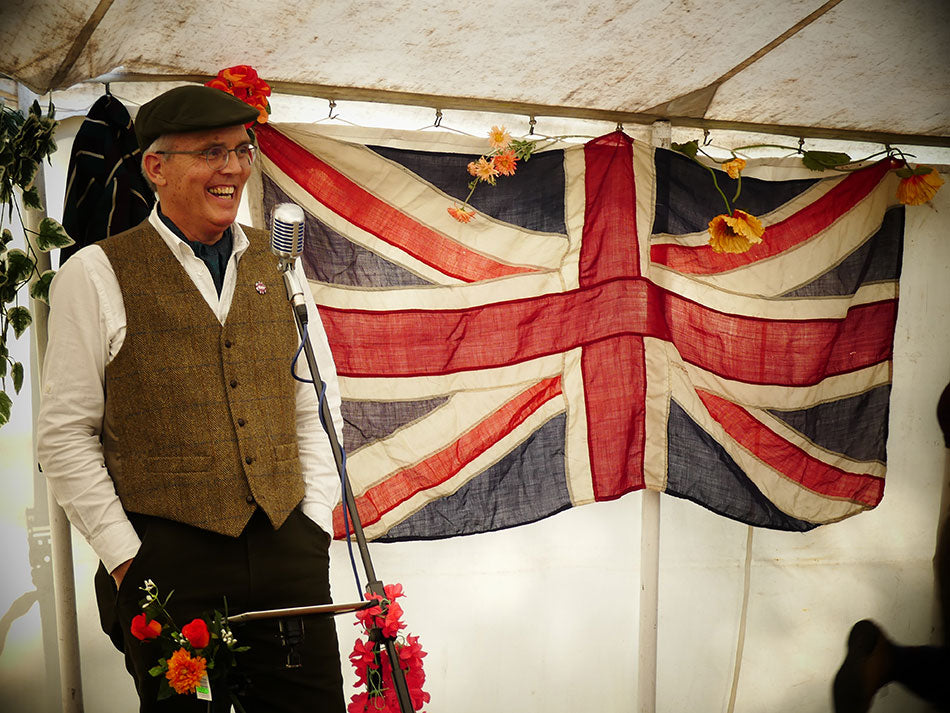 Pashley's MD, Adrian Williams, dressed in tweed and giving a speech at the Pashley Picnic Ride with a vintage union jack flag behind him.