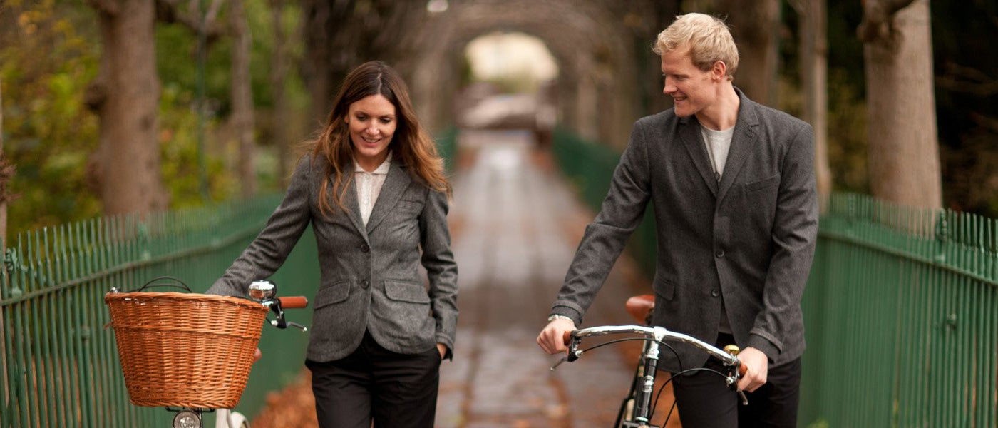 A couple wearing Pashley Tweed Blazer pushing their Pashley bicycles along a tree-lined pathway.