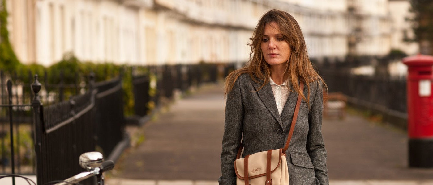A lady wearing a Pashley Tweed Blazer and Saddle Satchel next to a red post box in front of a crescent of houses.