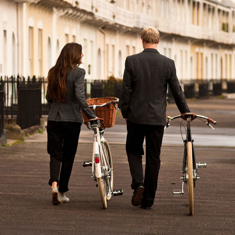 A couple dressed in tweed walking their Pashley bicycles in front of a row of houses in a crescent in Bristol.