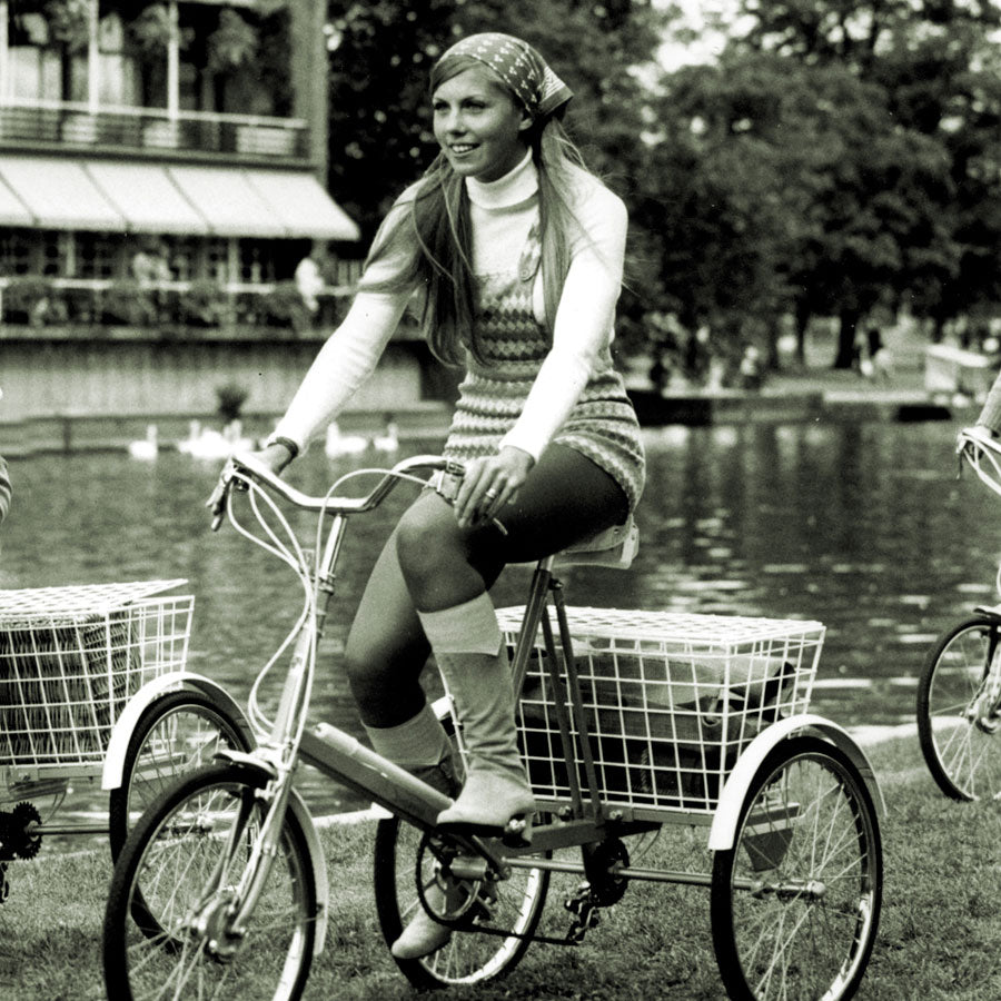 Young lady wearing 1960s fashion with a head scarf riding a Pashley tricycle along the river Avon.