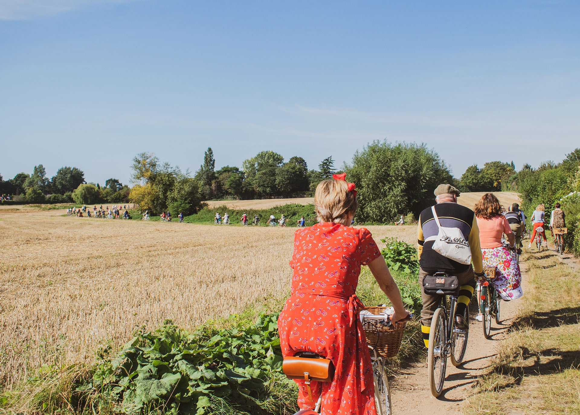 A group of cyclist dressed in vintage clothing riding along a country track on a bright summer's day.