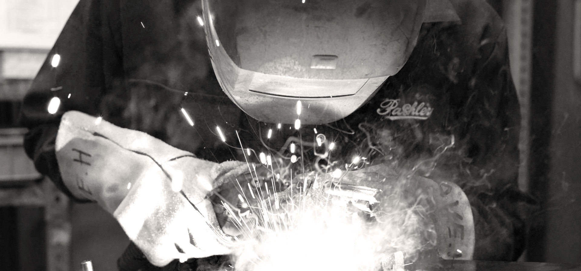 Pashley craftsman wearing a welding mask whilst fabricating a bicycle frame, with bright welding arc in the foreground.