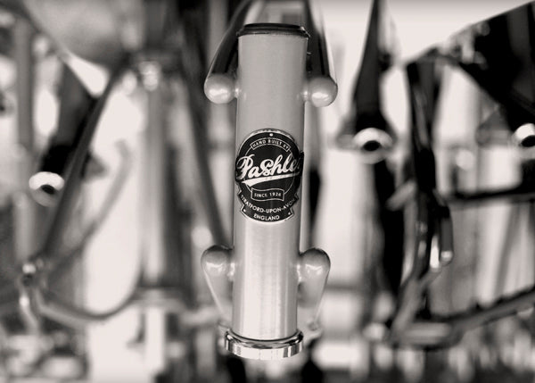 A close-up of a Pashley headbadge on the front of a bicycle frame hanging in a rack in the factory.