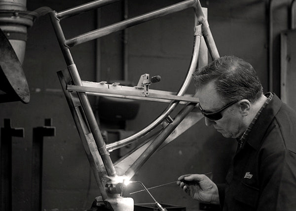 Pashley craftsman in overalls braising a bicycle frame that is in a jig.