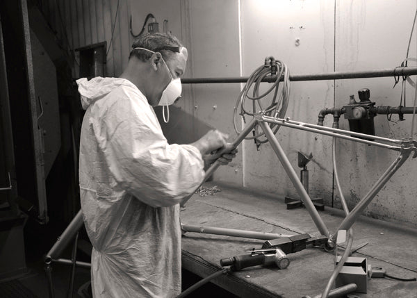 A man working on a bare bicycle frame, sanding it down before it goes to be painted.