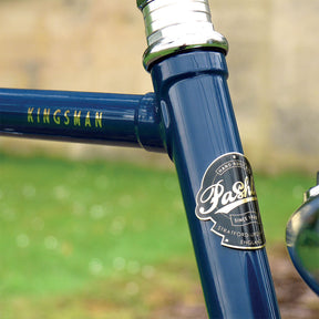 A close-up of the headbadge and top-tube graphic of the blue Kingsman bicycle.