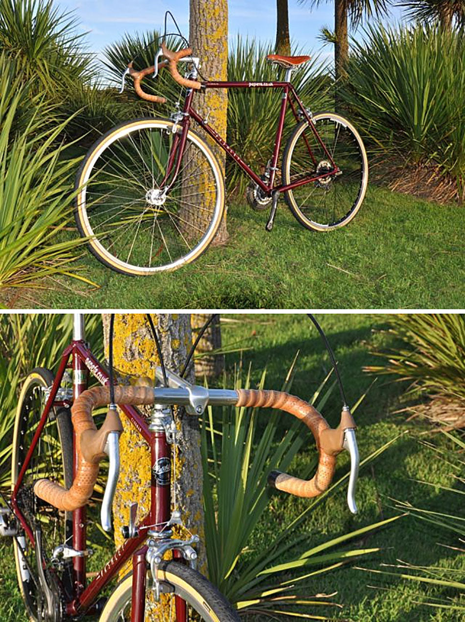The Pashley Clubman Country bicycle in Burgundy with tan brooks leather sandal and bar tape. It is leant next to a tree in a garden.