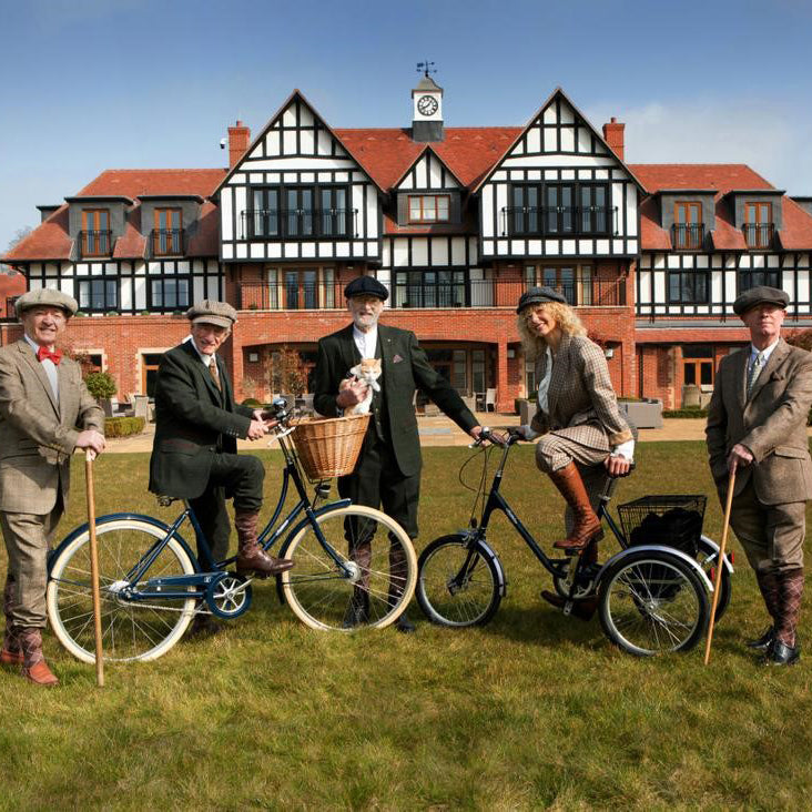 Five residents of Inspired Villages dressed in tweed posing alongside a Pashley Britannia ladies bike and a blue Pashley tricycle.