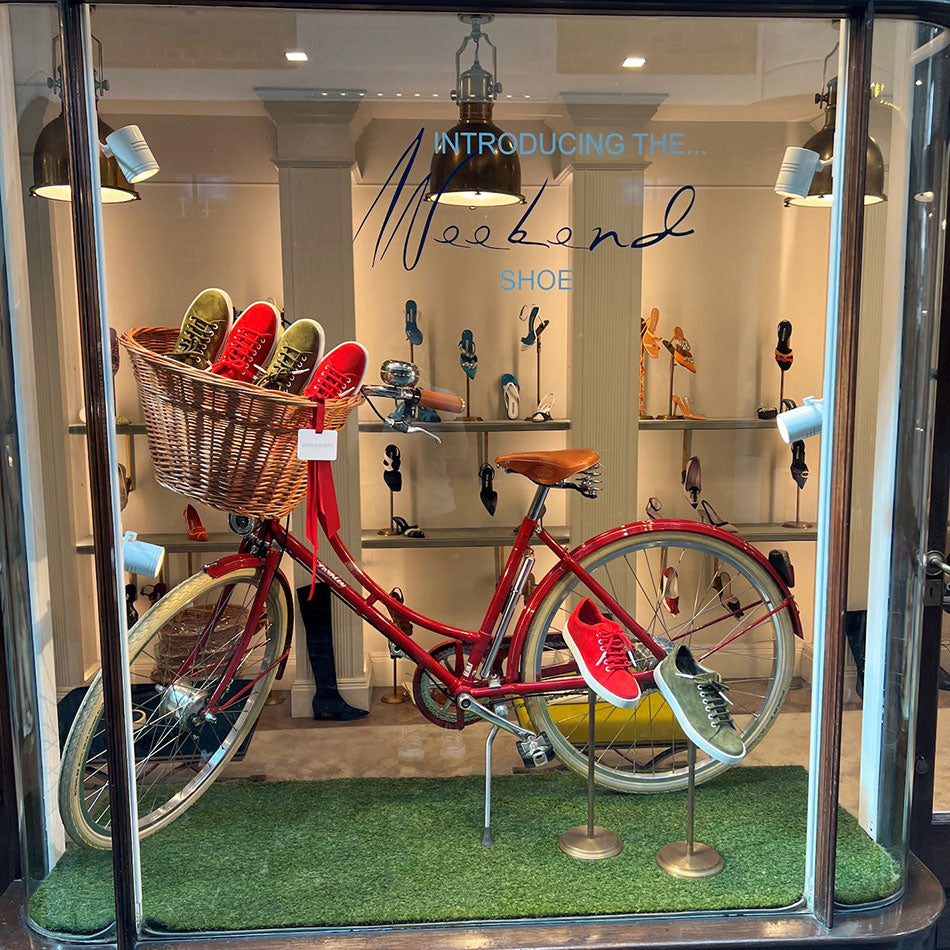 A bright red ladies vintage bike in a store window, with a wicker basket full of brightly coloured Manalo Blahnik sneakers.