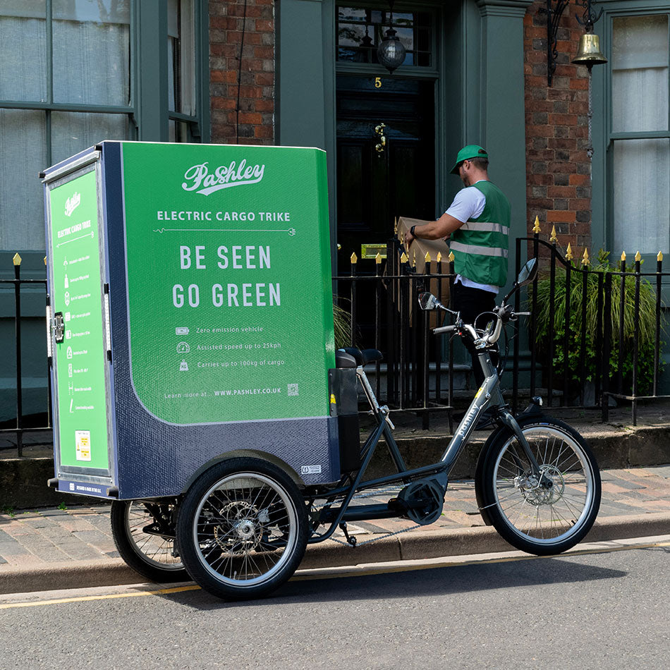Electric cargo trike parked on street with delivery rider in the background delivering a parcel.