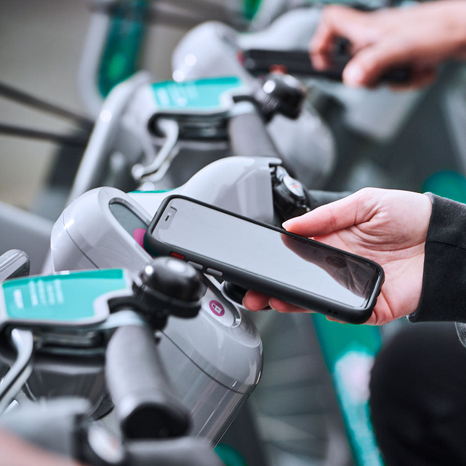 A person holding their mobile phone on a sensor on the handlebars of a hire bike to unlock it from its docking station.