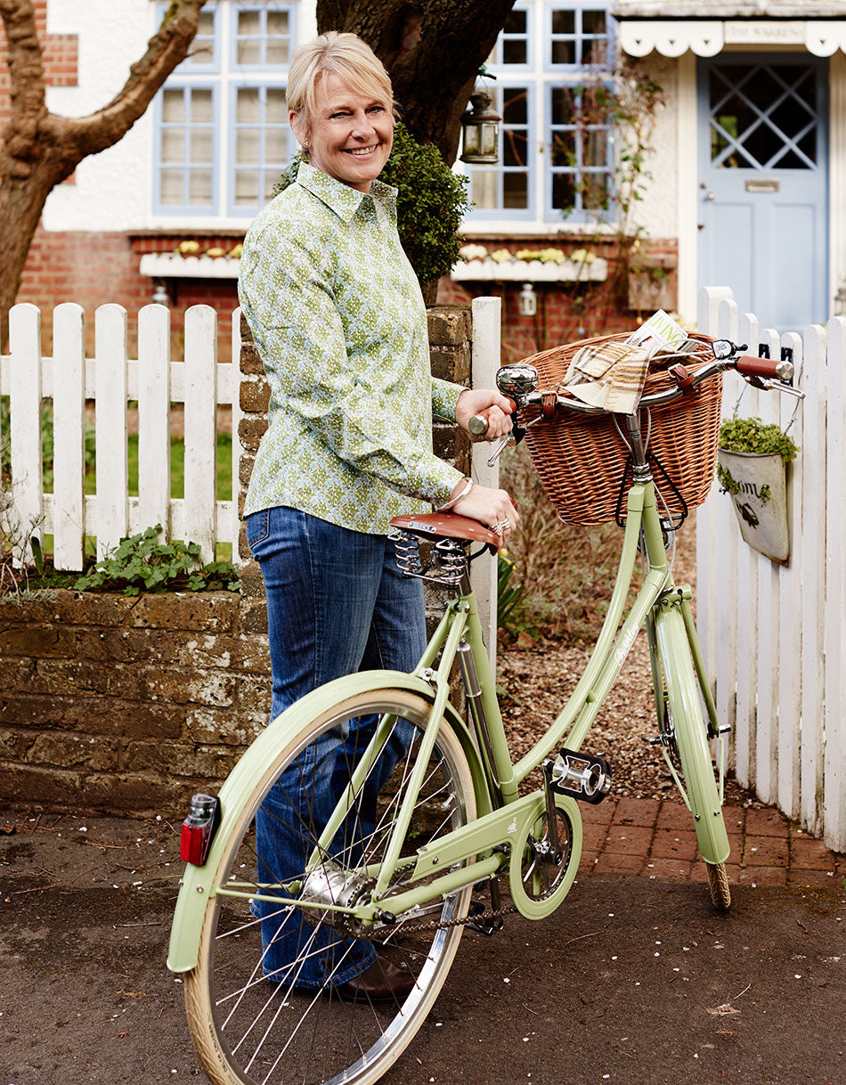 Country Living Editor Susy Smith with the Meadow Green ladies classic Pashley with wicker basket outside a cute cottage with a white picket fence.