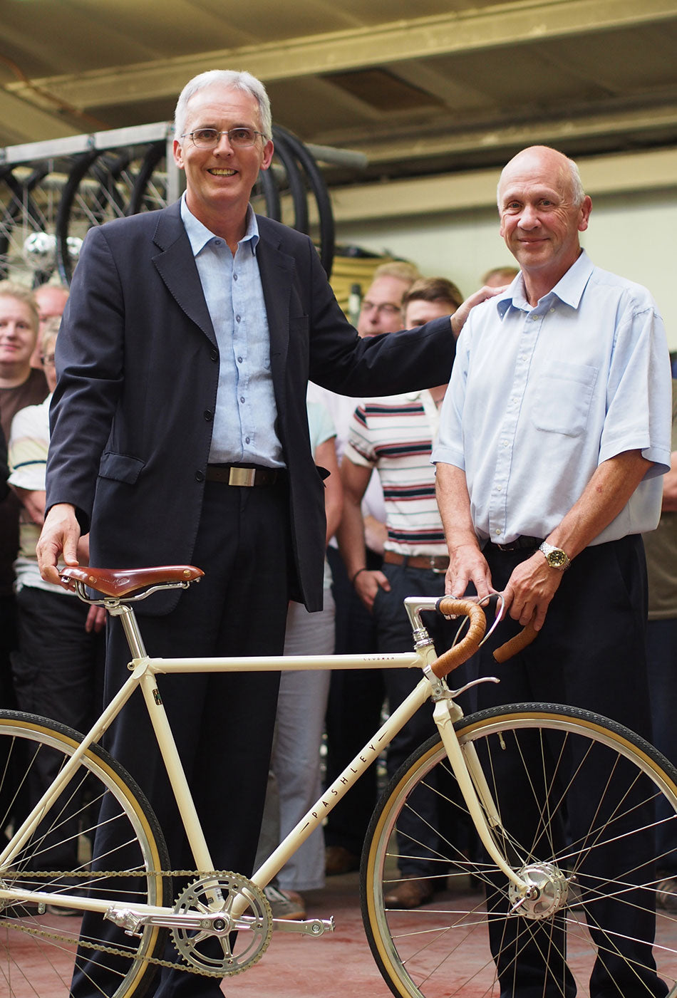 Adrian Williams standing next to John Kerby behind a Ivory colour Pashley Clubman classic road bike inside the Pashley factory.