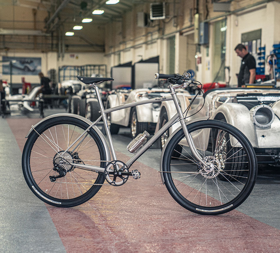 Silver Grey Pashley-Morgan 110 bike in the Morgan Motor factory with car production going on in the background.