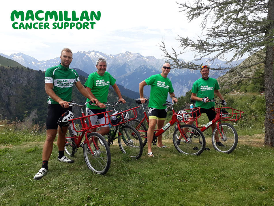 Postmen in green Macmillan charity t-shirts standing with their Pashley Pronto bicycles with the Alps in the background.