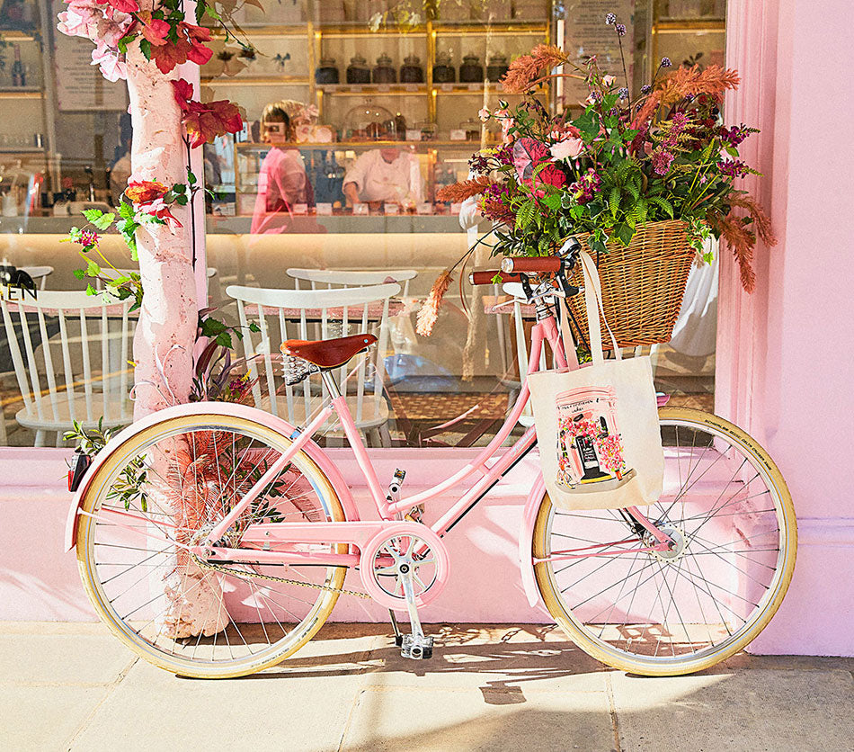 Pink classic Pashley ladies bicycle with a big bunch of colour flowers in its basket, sat outside the window a Peggy Porschen cake cafe in Chelsea.