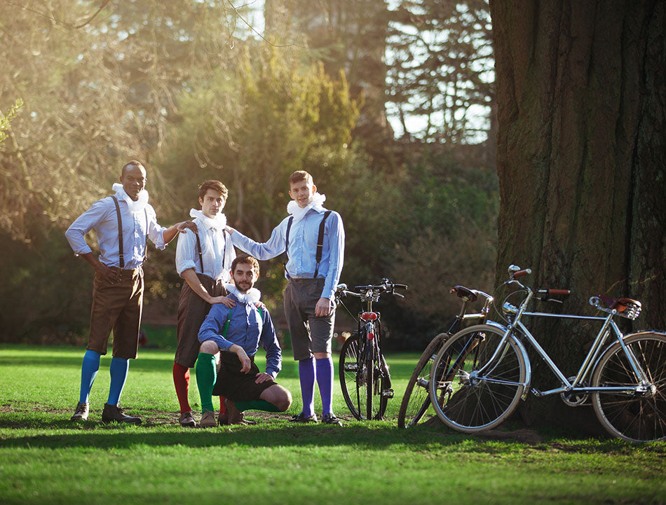 The HandleBards boys troupe dressed in plus fours, braces and neck ruffs, standing next to a silver Pashley Phantom Roadster bike in the park.