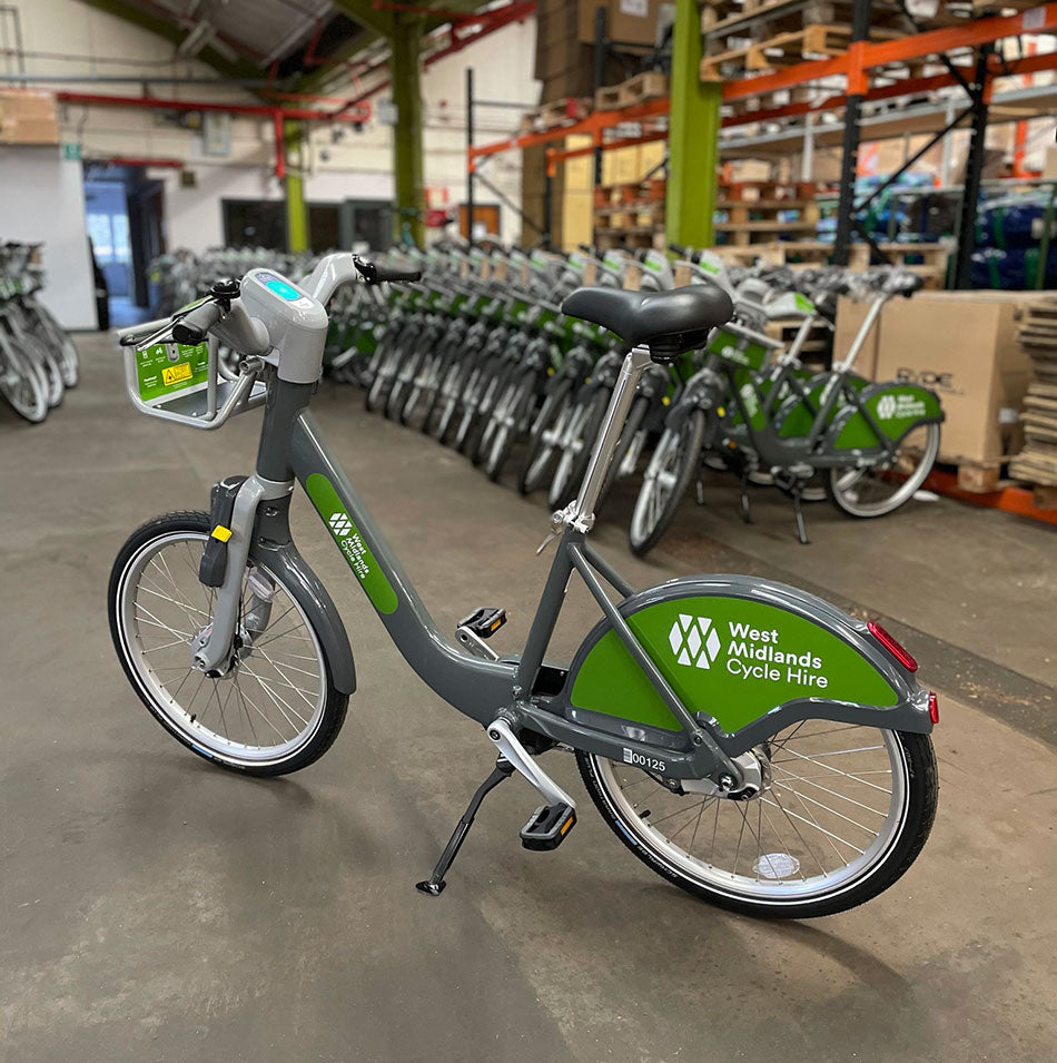A grey and green West Midlands Cycle bike standing inside the Pashley factory warehouse, with a rows more of them in the background.