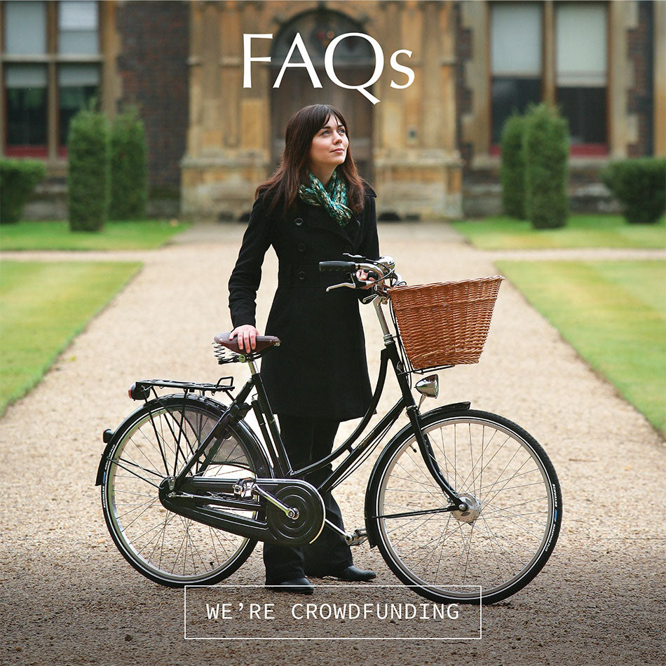 Lady standing in front of a stately home with a classic black bicycle with a large front wicker basket.