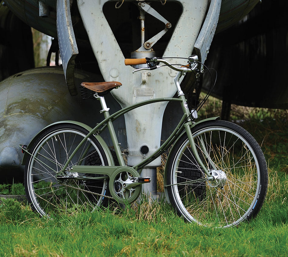 A green paratrooper style bicycle in front of an old aircraft standing on grass.