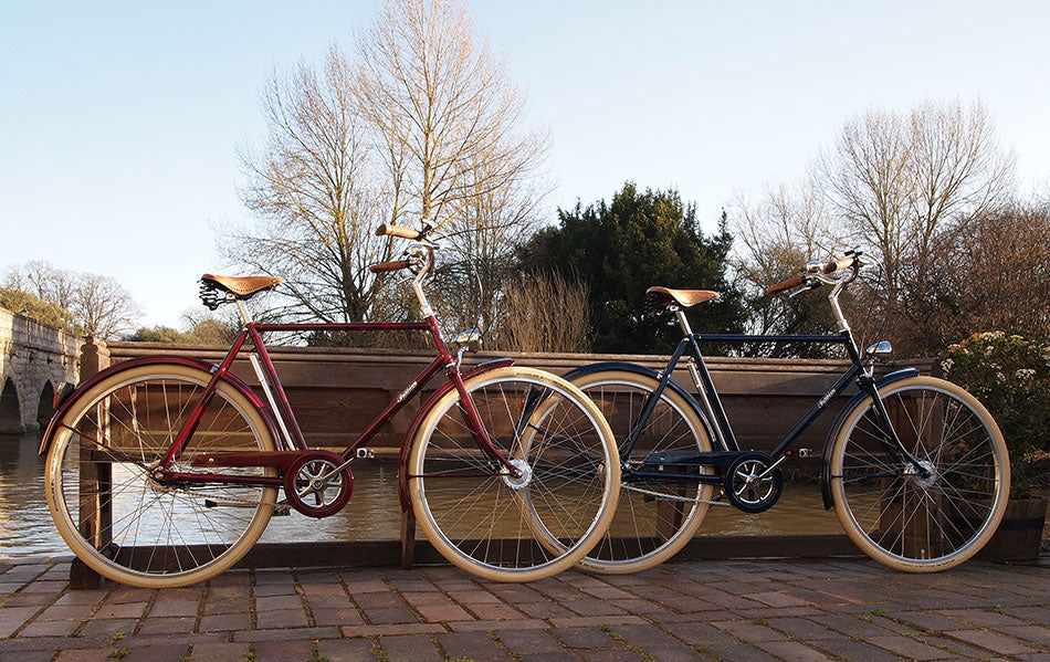 A pair of Pashley Briton bicycles - one red, one blue - sat alongside the river Avon in Stratford.