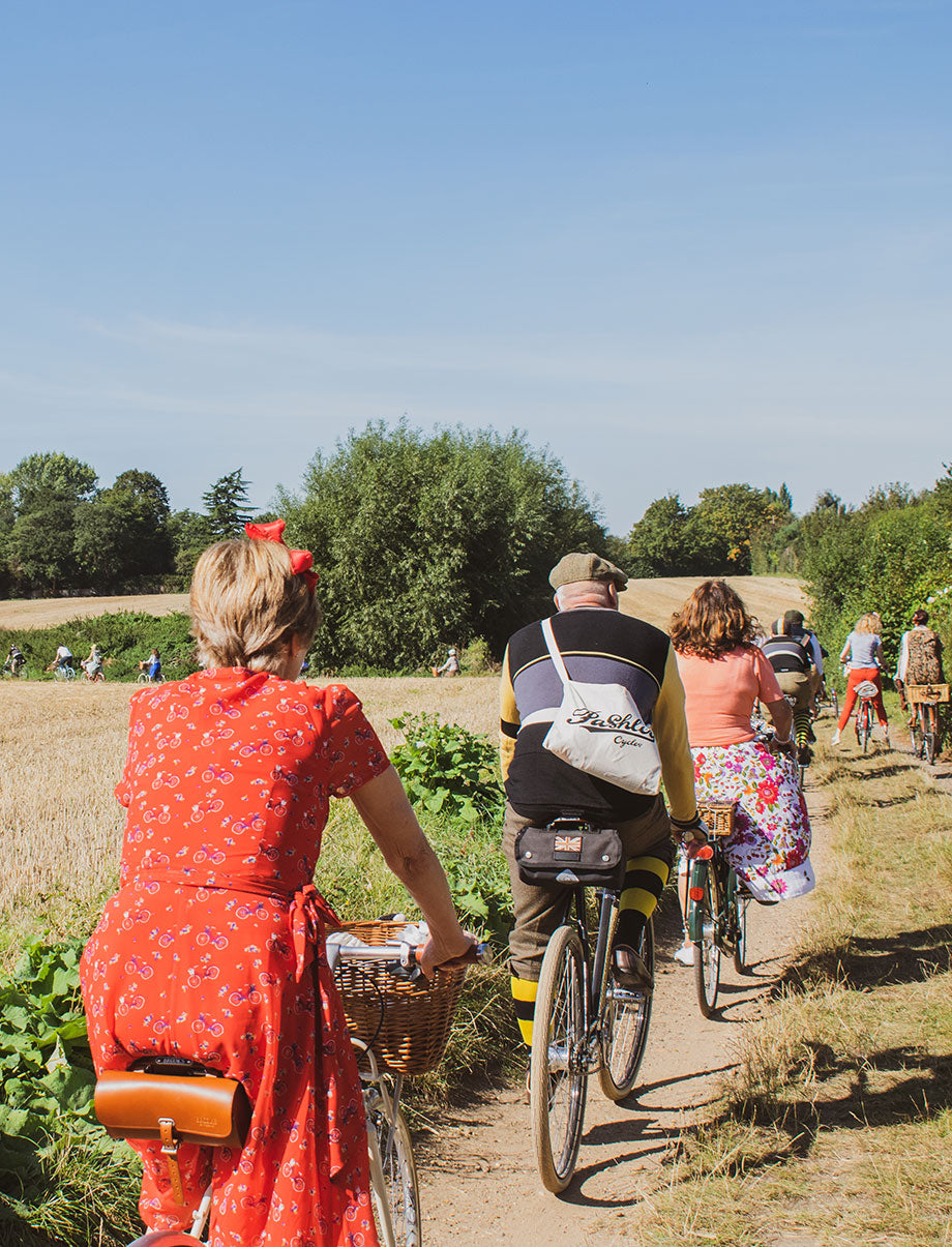 A group of cyclist dressed in vintage clothing riding along a country track on a bright summer's day.