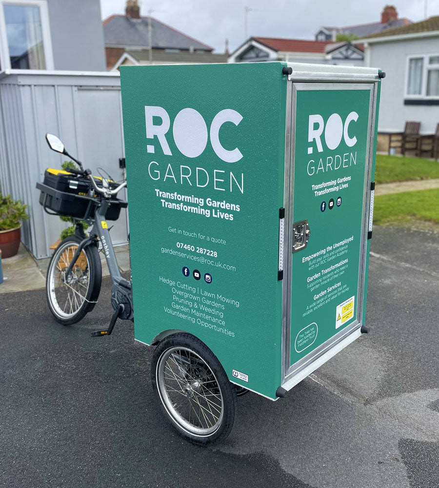 A electric cargo trike with branded rear post in front of a bungalow.