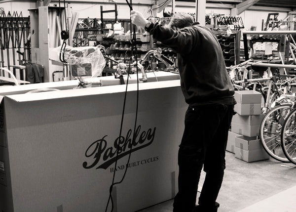 A man using a winch to lower a finished bike into its Pashley cardboard box ready for it to be shipped.