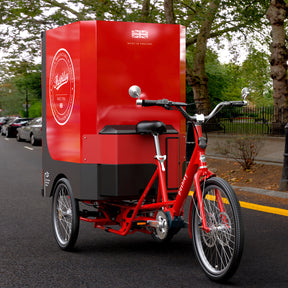 Red e-cargo trike with Pashley headbadge branding on the side of it's large, rear  cargo box.